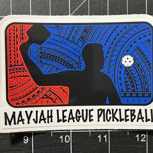 May include: A white sticker with a blue and red patterned design. The design features a silhouette of a person playing pickleball. The text "MAYJAH LEAGUE PICKLEBALL" is printed in black at the bottom of the sticker.