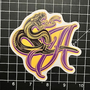 May include: A sticker with a purple and yellow design featuring a snake wrapped around a letter 'A'.