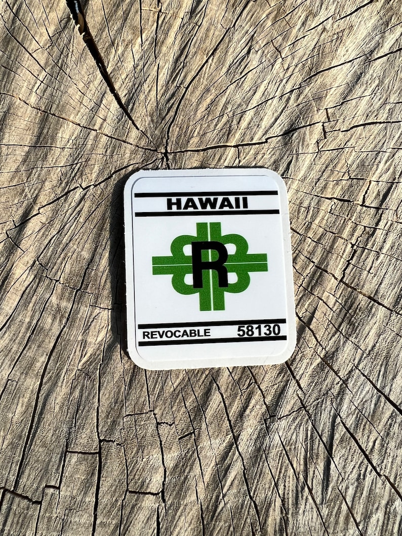 May include: White sticker with black text and green graphics. The sticker says "Hawaii" and "Revocable" with the number "58130". The graphic is a stylized letter "R" with a green cross on each side.
