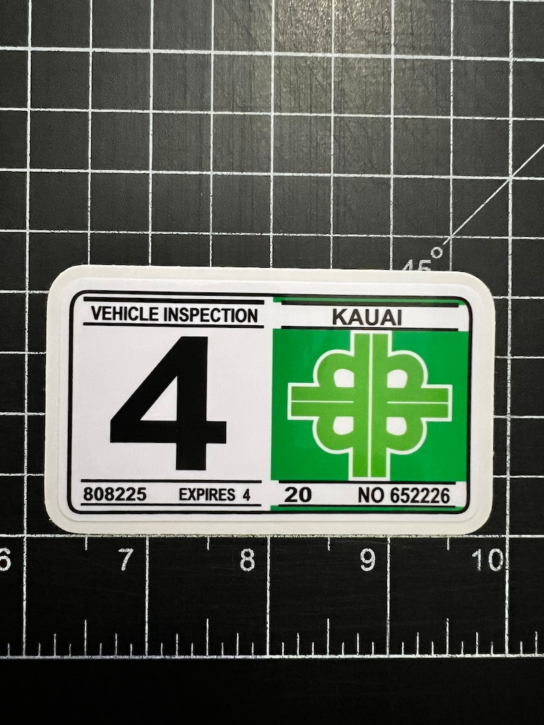 May include: A white sticker with green and black text and graphics. The sticker says "Vehicle Inspection" and "Kauai" with a green four-leaf clover symbol. The sticker also has the numbers "808225", "4", "20", and "652226".