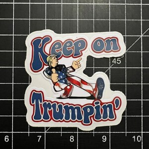 May include: A white sticker with a cartoon image of a person wearing a red, white, and blue outfit. The text "Keep on Trumpsin'" is in blue and red letters.