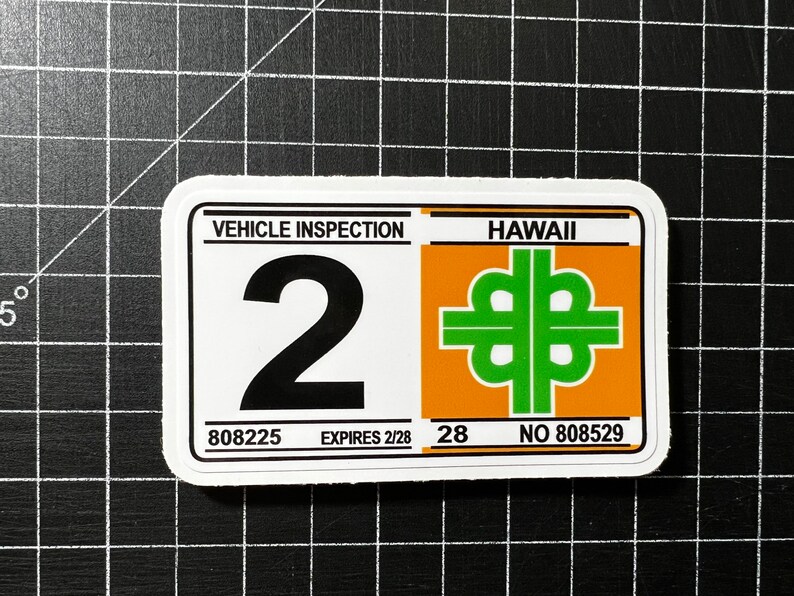 May include: White sticker with black text "VEHICLE INSPECTION" and a large black number "2". Below the number is "808225 EXPIRES 2/28". On the right side of the sticker is a green and orange symbol with the text "HAWAII 28 NO 808529"