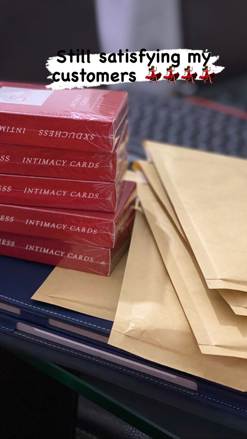 K&ouml;nnte beinhalten: Ein Stapel roter Boxen mit dem Text "INTIMACY CARDS" auf jeder Box. Die Boxen sind in Klarsichtfolie verpackt und liegen auf einem Stapel brauner Umschl&auml;ge.
