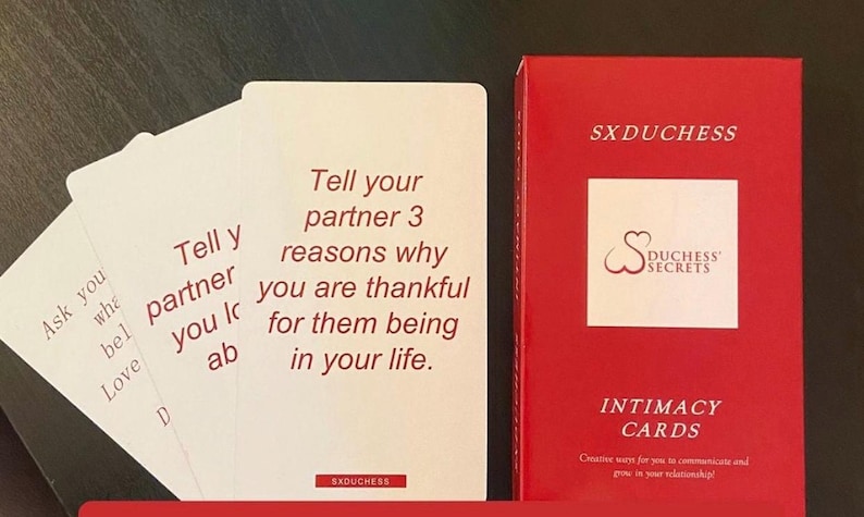 K&ouml;nnte beinhalten: Ein Set Intimit&auml;tskarten mit roter und wei&szlig;er Schrift auf wei&szlig;en Karten. Die Karten befinden sich in einer roten Schachtel mit dem Text "SXDUCHESS" und "DUCHESS SECRETS INTIMACY CARDS" auf der Vorderseite. Der Text auf den Karten lautet "Ask you what you believe Love D" und "Tell your partner 3 reasons why you are thankful for them being in your life. SXDUCHESS".