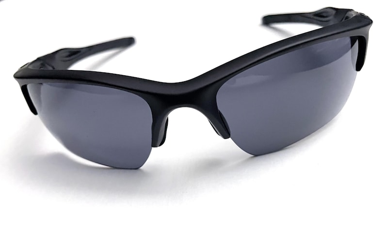 May include: Black sunglasses with gray lenses. The sunglasses have a sleek, modern design with a curved frame and a semi-rimless style. The lenses are a dark gray color, providing protection from the sun.