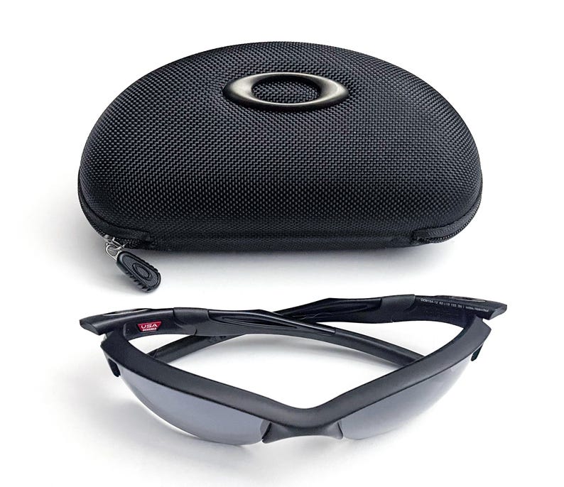 May include: Black sunglasses with a matching black case. The sunglasses have a sleek, modern design with dark lenses and a black frame. The case is oval-shaped with a zipper closure and the brand logo.