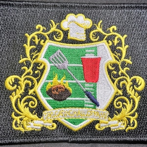 May include: Embroidered patch with a black background and a central crest design. The crest features a chef's hat, a football, a spatula, and a red cup, all set against a green field. The design is framed by gold filigree and a banner.