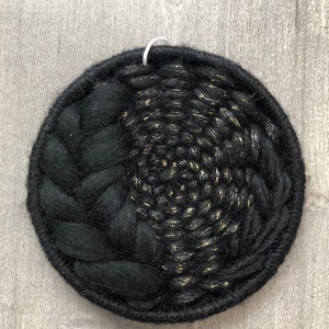 May include: Black and gold circular wall hanging made of woven yarn. The yarn is woven in a spiral pattern with a black yarn border.