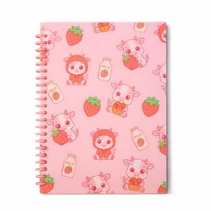 May include: Pink spiral-bound notebook with a repeating pattern of cartoon cows, strawberries, and milk bottles. The cows are wearing strawberry costumes. The notebook has a pink spiral binding.
