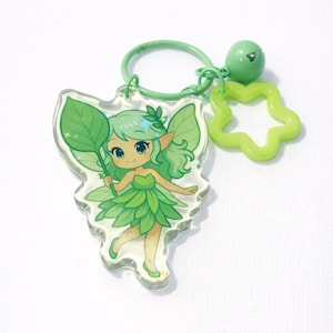 May include: A green fairy keychain with a leaf-shaped charm. The fairy has green hair and a leaf dress, holding a leaf. A green flower and a small bell dangle from the keychain ring.
