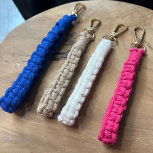 Puede incluir: Cuatro llaveros con cordones trenzados de diferentes colores y cierres de metal dorado. Los cordones son azul, beige, blanco y rosa.