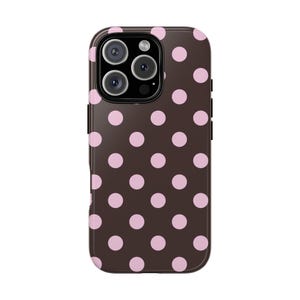 Pode incluir: Uma capa de telefone castanha com um padrão de bolinhas rosa espaçadas. A capa tem um acabamento brilhante e apresenta um módulo de câmara com várias lentes. O design é simples e clássico, adequado para vários estilos.
