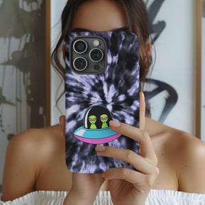 K&ouml;nnte beinhalten: Smartphone-H&uuml;lle mit einem Batikmuster in Schwarz und Lila. Die H&uuml;lle zeigt eine Cartoon-Illustration eines UFOs mit zwei gr&uuml;nen Au&szlig;erirdischen. Das UFO hat einen blauen und rosa Rand.