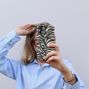 K&ouml;nnte beinhalten: Eine Person h&auml;lt eine schwarze und wei&szlig;e Handyh&uuml;lle mit Zebra-Muster vor ihrem Gesicht. Die H&uuml;lle ist f&uuml;r ein iPhone.