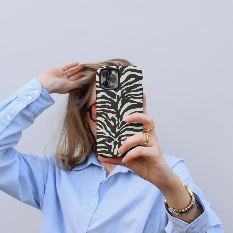 K&ouml;nnte beinhalten: Eine Person h&auml;lt eine schwarze und wei&szlig;e Handyh&uuml;lle mit Zebra-Muster vor ihrem Gesicht. Die H&uuml;lle ist f&uuml;r ein iPhone.
