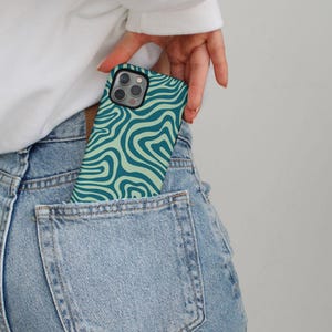 May include: A green and light green phone case with a wavy pattern. The case is in a back pocket of blue jeans. GRACIE Groovy Protective | Trendy | Cute | Aesthetic | Stylish | Sleek | Chic | iphone case | iphone