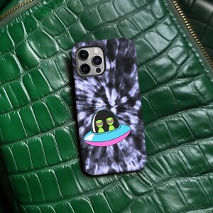 K&ouml;nnte beinhalten: Handyh&uuml;lle mit einem schwarz-wei&szlig;en Batikmuster. Auf der H&uuml;lle ist eine Cartoon-Grafik eines UFOs mit zwei gr&uuml;nen Aliens abgebildet. Das UFO ist rosa und blau umrandet.