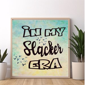 May include: A framed print with a watercolor background in shades of blue and yellow. The print features the text "In my Slacker ERA" in black lettering.