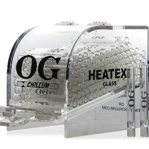 Op de afbeelding: Een transparante acryl display met een collectie glazen buizen. De display heeft de tekst "OG Chillum" en "HEATEX GLASS" erop gedrukt. Twee glazen buizen worden buiten de display getoond.