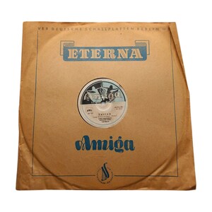Könnte beinhalten: Eine braune Papier-Plattenhülle mit dem Text "VEB Deutsche Schallplatten Berlin W" und "ETERNA" auf der Vorderseite. Die Hülle hat ein blaues und weißes Plattenlabel mit dem Text "Amiga" und "Zarina" darauf.