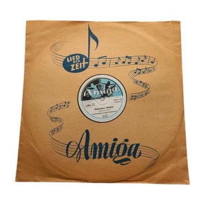 Könnte beinhalten: Eine braune Papier-Plattenhülle mit einem blauen und weißen Plattenlabel. Das Label trägt den Text "Amiga" und "Schwedan - Modal". Die Hülle hat ein blaues Musiknoten-Design mit dem Text "Lied der Zeit" darauf.