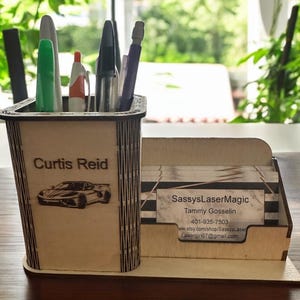 May include: Wooden desk organizer with a personalized name "Curtis Reid" and a small car design. The organizer has a separate compartment for business cards with the text "SassyLaserMagic, Tammy Gosselin, 401-935-7503, www.etsy.com/shop/SassyLaserMagic, lasergirl67@gmail.com".