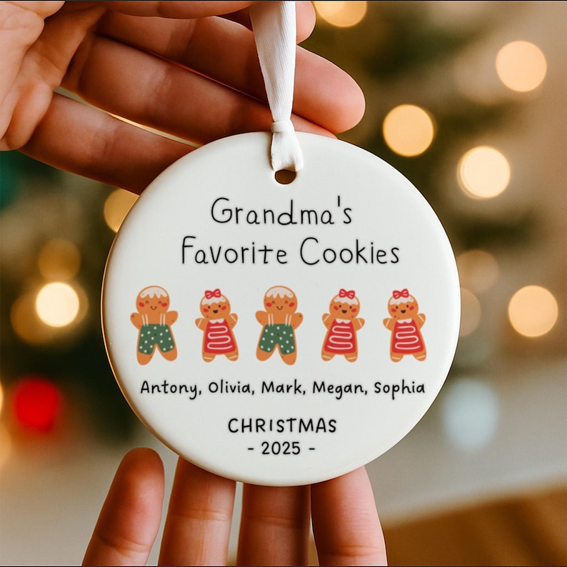 Peut inclure: Une d&eacute;coration ronde en c&eacute;ramique blanche avec le texte Grandma's Favorite Cookies, cinq illustrations de bonshommes en pain d'&eacute;pices, les pr&eacute;noms Antony, Olivia, Mark, Megan, Sophia et le texte CHRISTMAS - 2025, suspendue par un ruban blanc.