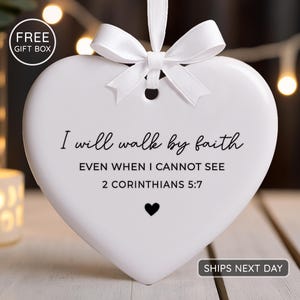 May include: A white heart-shaped ornament with a white ribbon and bow. The ornament has the text "I will walk by faith" and a Bible verse. A small black heart is below the text.