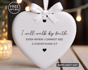 May include: A white heart-shaped ornament with a white ribbon and bow. The ornament has the text "I will walk by faith" and a Bible verse. A small black heart is below the text.