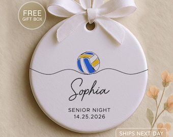 May include: A round white ceramic ornament featuring a blue and yellow volleyball graphic above a black wavy line. The name Sophia is printed in black script, followed by the text SENIOR NIGHT and the date 14.25.2026. A white ribbon is tied at the top.