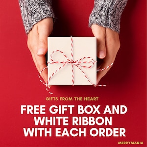 Peut inclure: Une bo&icirc;te cadeau carr&eacute;e blanche nou&eacute;e avec un ruban en ficelle bicolore rouge et blanc. Le texte indique : GIFTS FROM THE HEART, FREE GIFT BOX AND WHITE RIBBON WITH EACH ORDER, MERRYMANIA. Le fond est d'une couleur rouge unie.