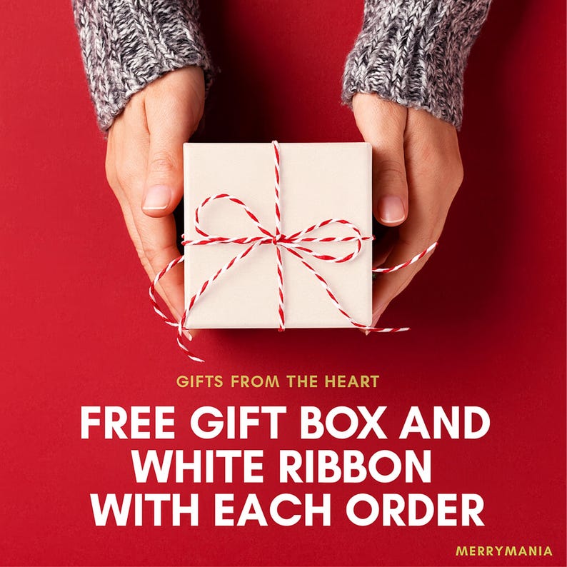 Peut inclure: Une bo&icirc;te cadeau carr&eacute;e blanche nou&eacute;e avec un ruban en ficelle bicolore rouge et blanc. Le texte indique : GIFTS FROM THE HEART, FREE GIFT BOX AND WHITE RIBBON WITH EACH ORDER, MERRYMANIA. Le fond est d'une couleur rouge unie.