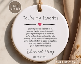 May include: A round white ceramic ornament hanging from a jute twine loop. The text reads: You're my favorite, followed by a list of sentiments, the names Olivia and Henry, and the date 01.28.2026. A small pink heart is centered below the title.