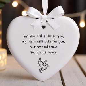 May include: A white heart-shaped ornament with a white ribbon and bow. The ornament has the text "my mind still talks to you, my heart still looks for you, but my soul knows You are at peace." and a dove illustration.