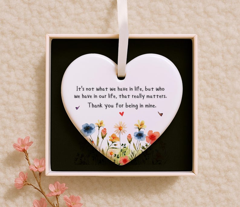 May include: A white heart-shaped ornament with a ribbon for hanging, presented in a box. The ornament features a floral design at the bottom and a heartfelt message: "It's not what we have in life, but who we have in our life, that really matters. Thank you for being in mine."