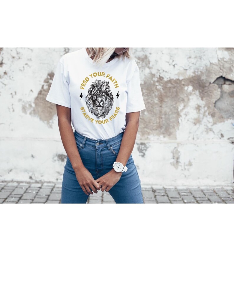 May include: White t-shirt with a graphic of a lion's head and the text "Feed Your Faith Starve Your Fears".