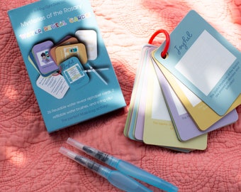 May include: A set of "Mysteries of the Rosary" water reveal cards with a box, a ring clip, and two refillable water brushes. The cards are in pastel colors and have the word "Joyful" on one. The box reads "Shining Light Dolls LLC".