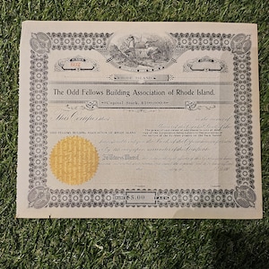 May include: An antique stock certificate from the Odd Fellows Building Association of Rhode Island. The document features ornate borders, a gold seal, and detailed text. The certificate states "Capital Stock, $100,000." and "Shares $5.00 Each."