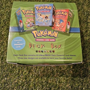 May include: A green Pokémon Trading Card Game Deck Box with three smaller deck boxes on top. The smaller boxes feature different Pokémon characters and the text "Deck Box". The main box reads "Contains no Pokémon cards."