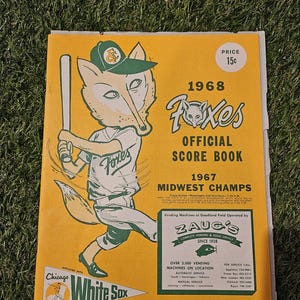 Może przedstawiać: Oficjalna książka wyników z 1968 roku dla drużyny baseballowej Appleton Foxes, w kolorze żółtym i zielonym. Na okładce znajduje się kreskówkowy lis w stroju baseballowym trzymający kij. Książka jest powiązana z Chicago White Sox. Książka zawiera również informacje o mistrzostwach Midwest z 1967 roku i automatach na Goodland Field obsługiwanych przez Zaug's Complete Vending & Food Service.