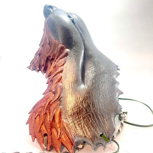 May include: A silver and copper wolf mask with a textured fur design. The mask is attached to a green and white cord.