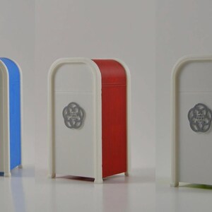 May include: Three rectangular, white containers with rounded tops and colored sides in blue, red, and green. Each has a silver emblem on the front. The containers are on a white surface.