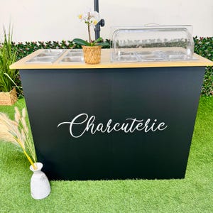 Pu&ograve; includere: Una stazione di servizio per salumi nera con un piano in legno chiaro. La stazione ha contenitori per alimenti in acciaio inossidabile e un coperchio in plastica trasparente. La parola "Charcuterie" &egrave; scritta in bianco sul davanti. Un'orchidea in vaso &egrave; in cima.