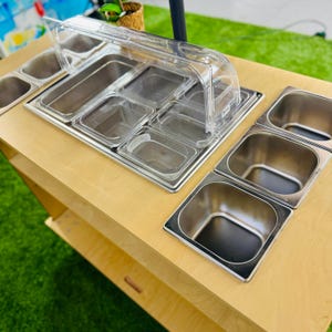 May include: A wooden food cart with multiple stainless steel food containers. The cart has a clear plastic lid to cover the containers.