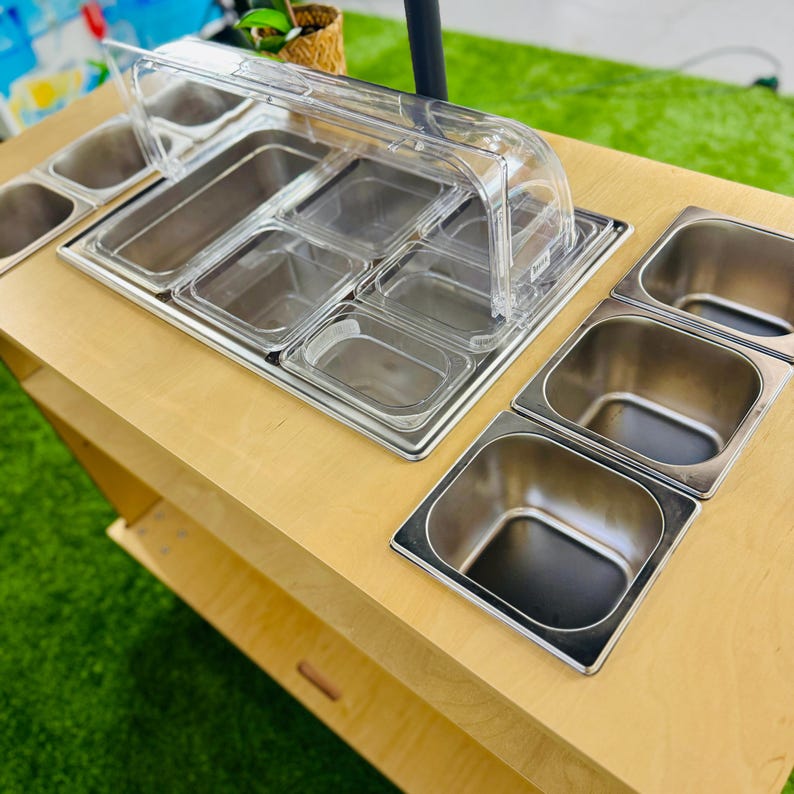 May include: A wooden food cart with multiple stainless steel food containers. The cart has a clear plastic lid to cover the containers.