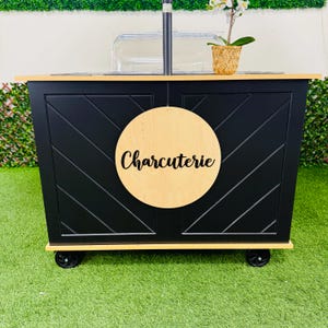 May include: Black wooden cart with wheels, a clear plastic container, and a wooden sign that says "Charcuterie".