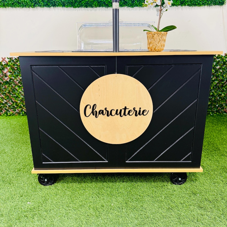 May include: Black wooden cart with wheels, a clear plastic container, and a wooden sign that says "Charcuterie".