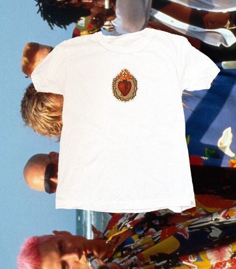 May include: White t-shirt featuring a graphic of a red heart with a crown of thorns and flames on a white background.