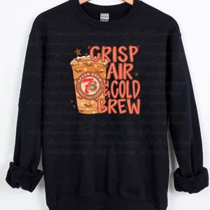 May include: A black long-sleeve sweatshirt featuring a graphic of a coffee cup with the text "SEVEN BREW DRIVE THRU COFFEE" and the words "CRISP AIR & COLD BREW" in orange and red lettering, accented with small stars and bat silhouettes.