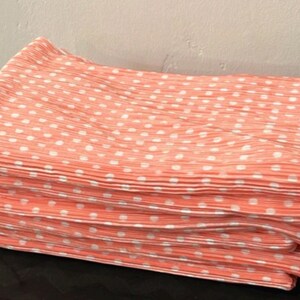 May include: A stack of four coral pink fabric napkins with white polka dots. The napkins are folded and have a pleated texture.